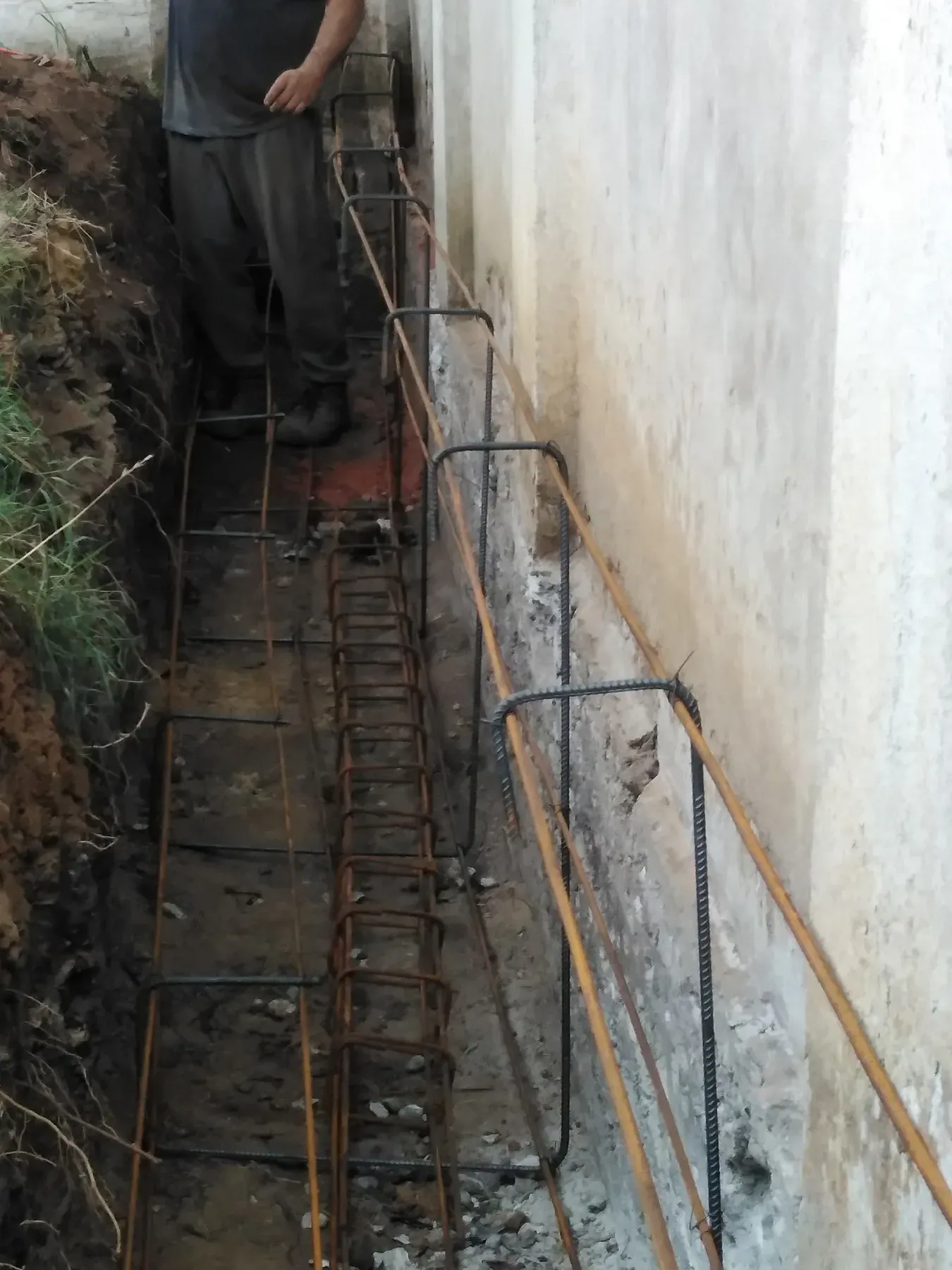 Zanja lineal con armadura de acero junto a un muro existente.